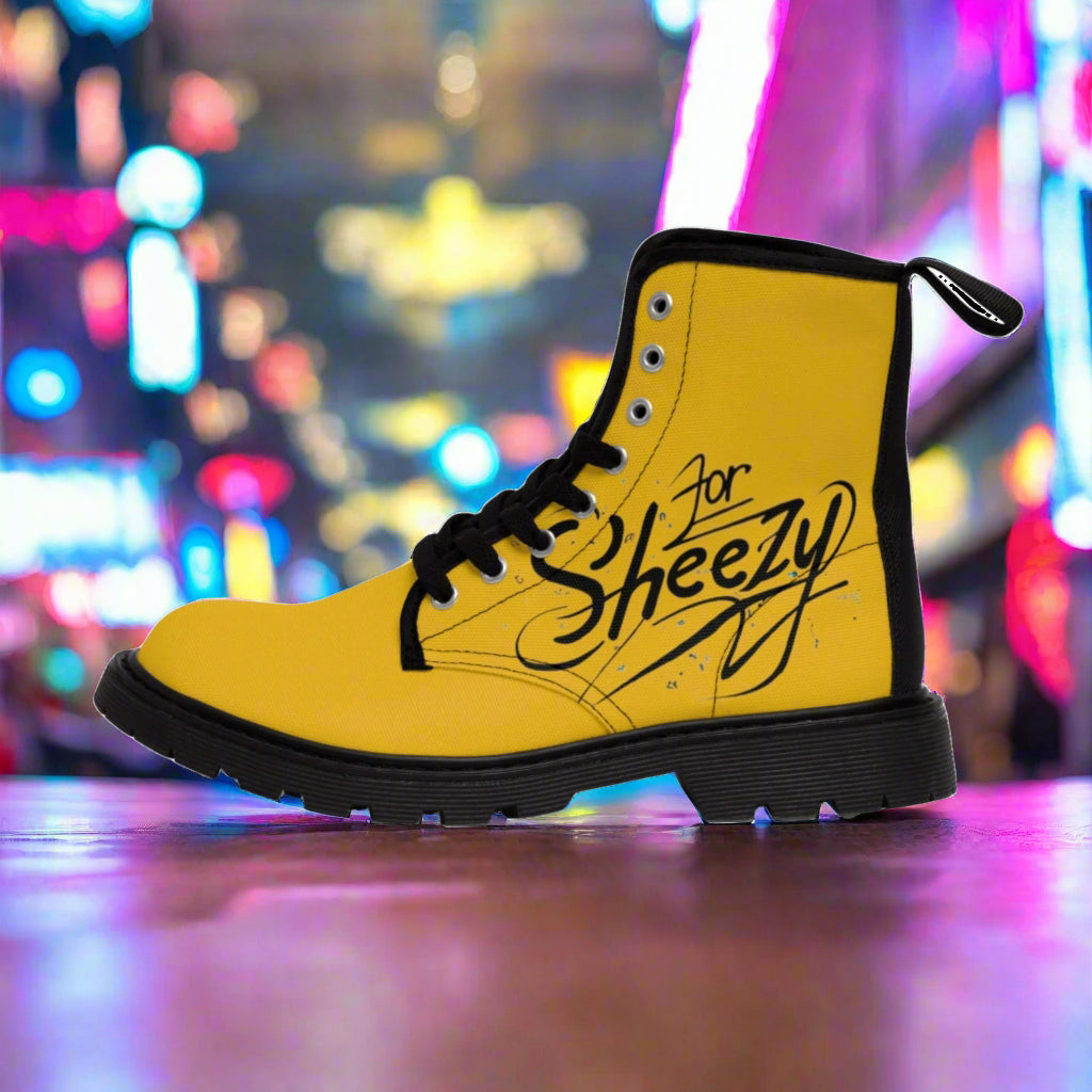 Yellow combat boot with black laces and a black sole, featuring the words 'For Sheezy' in a bold, stylized script on the side, set against a vibrant urban background with colorful neon lights.
